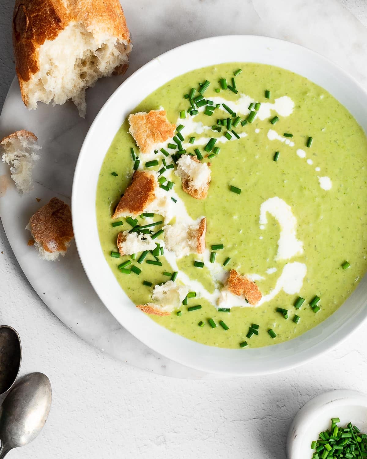 Asparagus soup in a white bowl, garnished with fresh cream, chives and sourdough bread.
