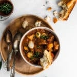 beef and bacon stew served with a crusty piece of bread in a white bowl