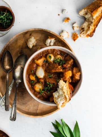 beef and bacon stew served with a crusty piece of bread in a white bowl