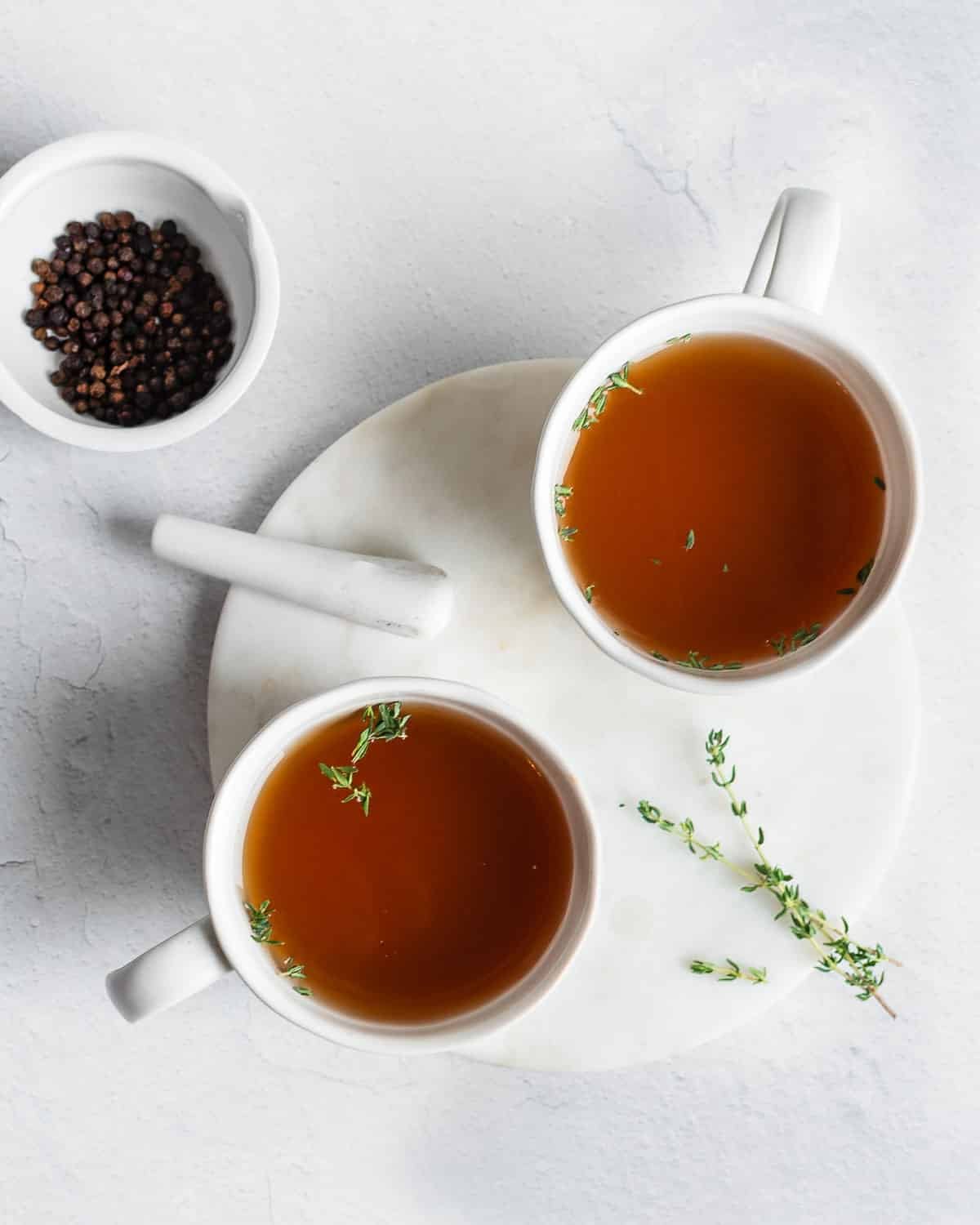 Beef bone broth in white mugs, garnished with frsh thyme