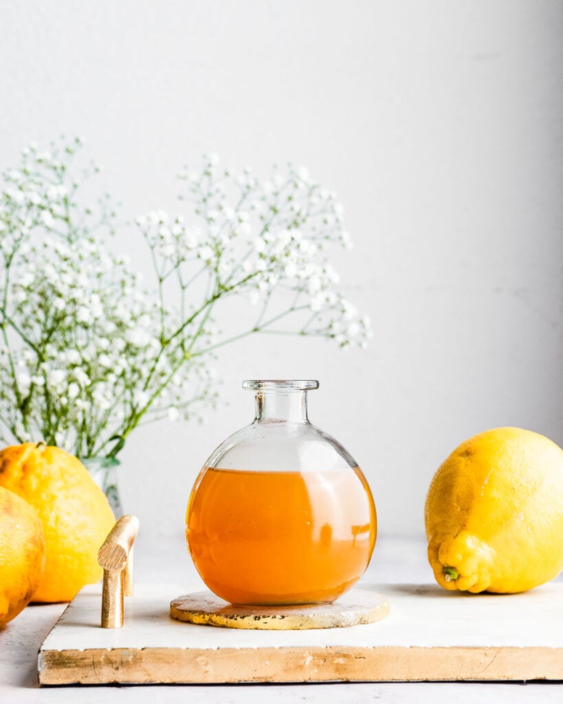 Bergamot orange syrup in a glass bottle on a tray next to fresh bergamot oranges.