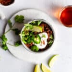 Bison chili in a stoneware bowl garnished with jalapenos, sour cream, green onions, and lime