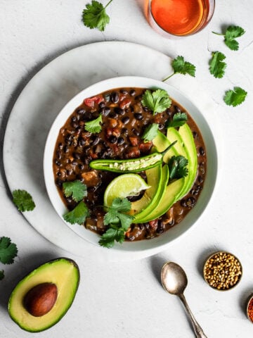 Black bean soup with chicken in a bowl, garnished with cilantro, lime, avocado and serrano chili