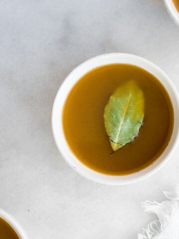 Bone Broth in a white bowl garnished with bay leaf