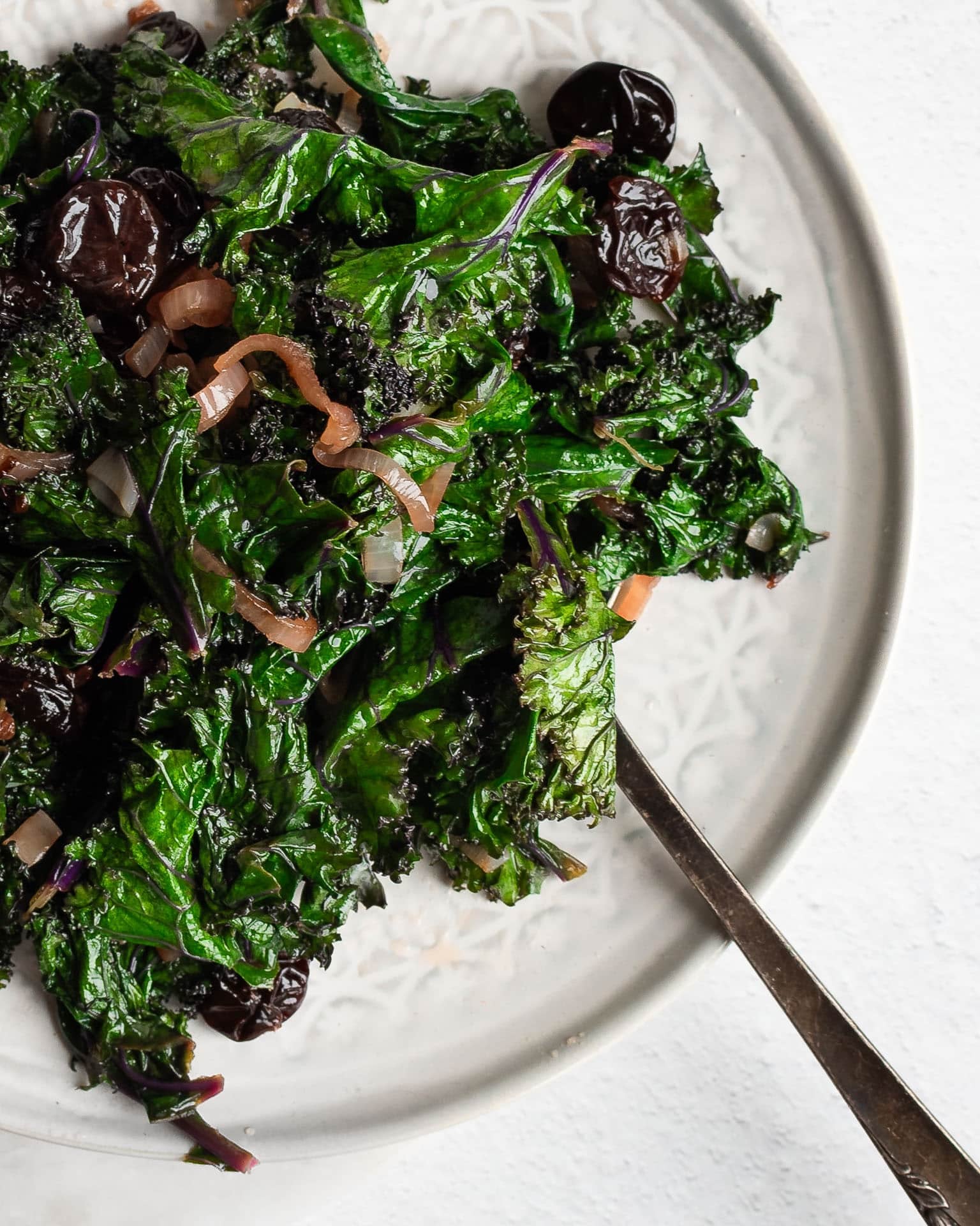 braised kale with cherries on a white plate