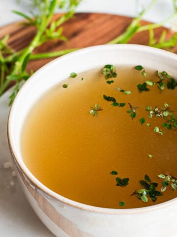 broth in a white bowl garnished with fresh thyme leaves