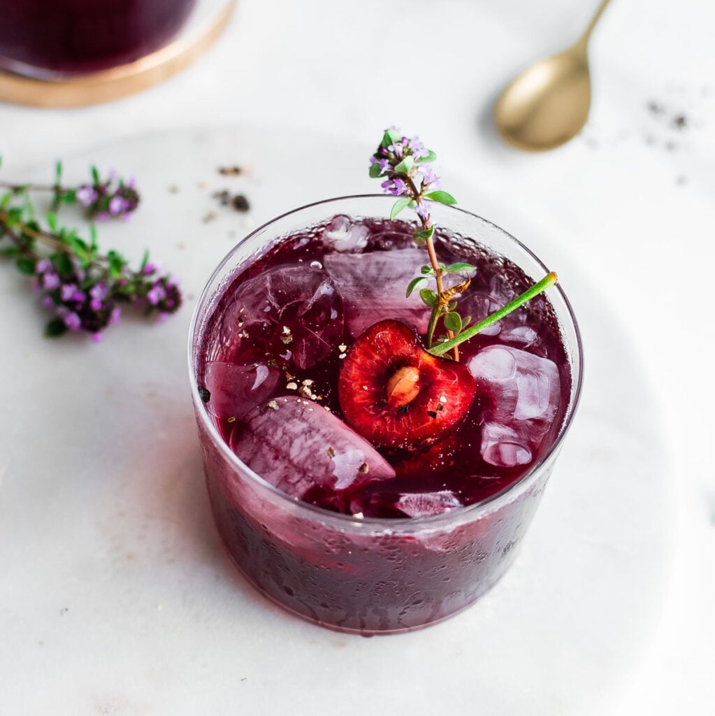 Cherry shrub served over ice garnished with black cherry, thyme, and black pepper