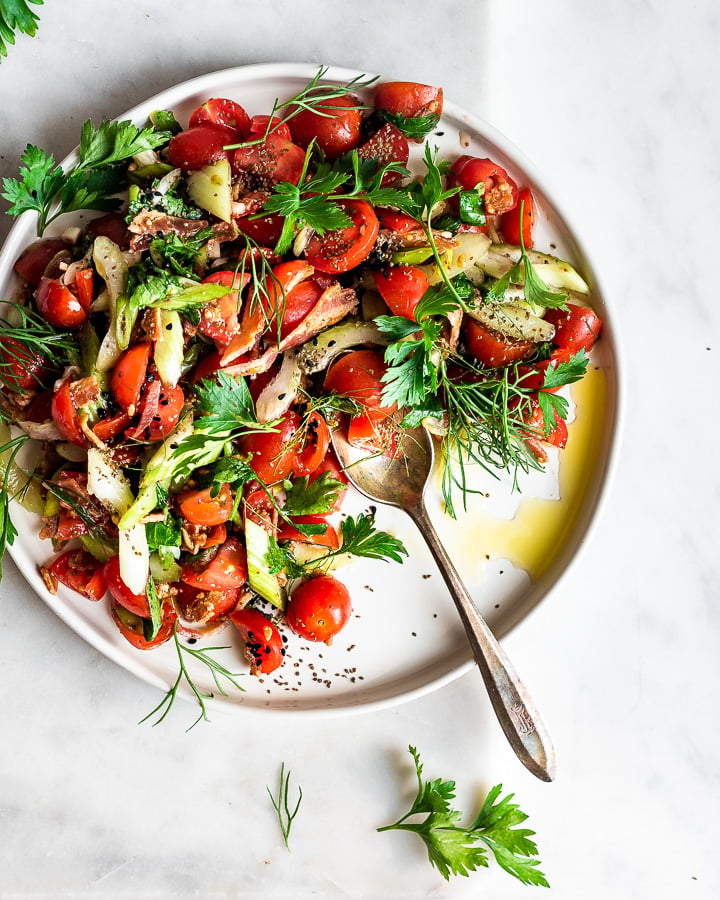 Herb-packed cherry tomato salad on a plate shot from overhead.