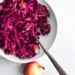 cider-braised cabbage in a white bowl, apples in background