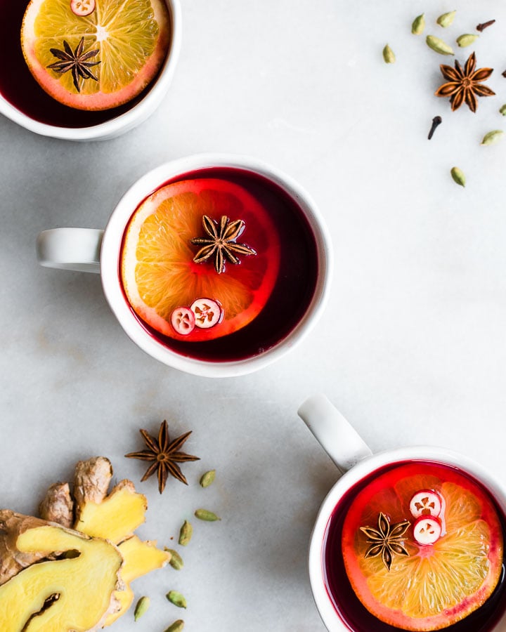 Three cups of cranberry cider garnished with orange slices, fresh cranberries and star anise.
