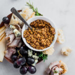 fermented mustard in a small bowl next to grapes cheese crackers and rosemary