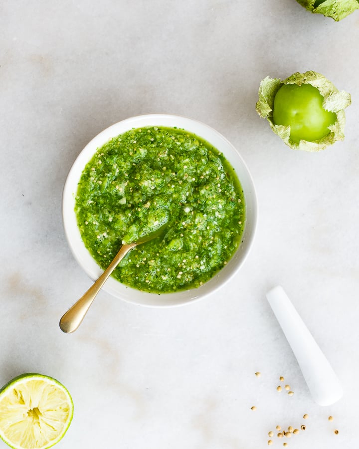 Fermented salsa in a bowl next to lime, tomatillos and coriander seed.