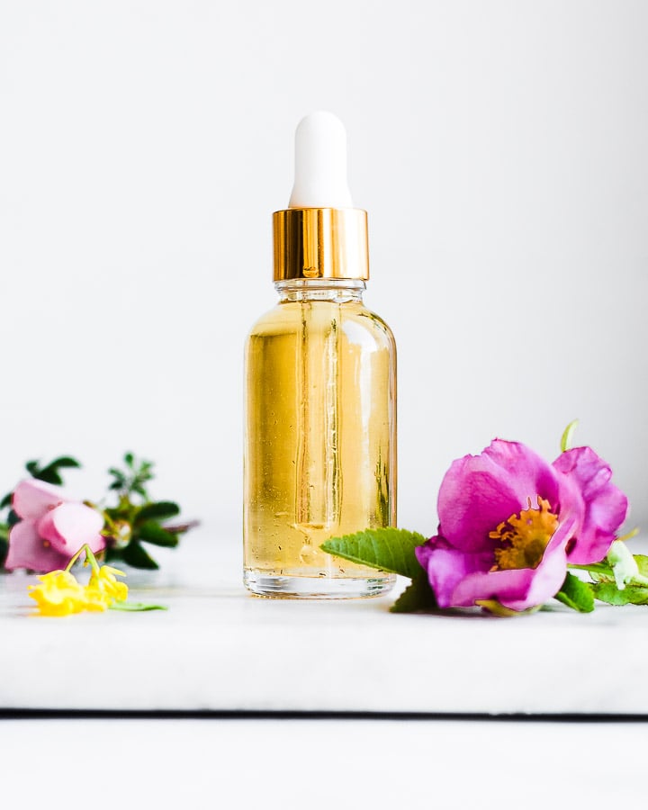 Homemade flower essence in a glass dropper bottle next to rose blossoms and mustard flowers.