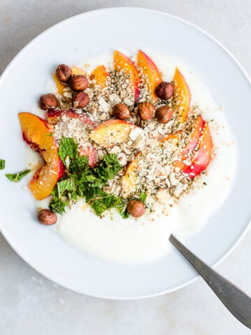Bowl of homemade yogurt garnished with nectarines, mint, hemp seeds and almonds