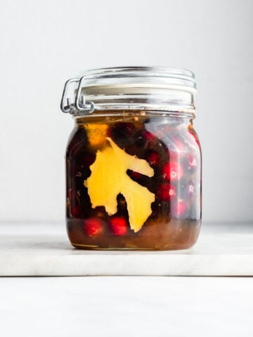 Fresh cranberries and sliced fresh ginger in a honey-filled fido jar on a marble surface