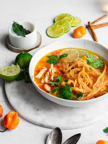 Lime soup in white bowl, garnished with cilantro, habanero peppers and lime
