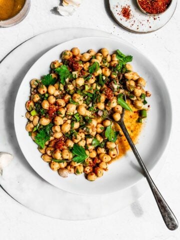 Marinated chickpeas in a white bowl garnished with chili powder, green onion, and parsley