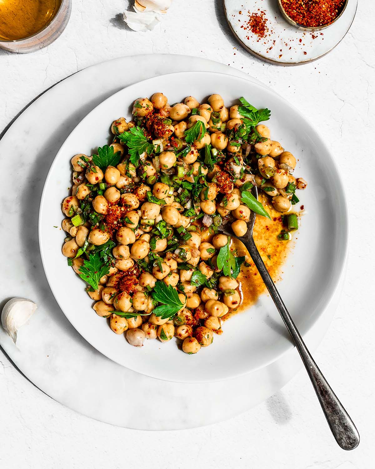 Marinated chickpeas in a white bowl garnished with chili powder, green onion, and parsley