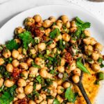 Marinated chickpeas in a white bowl garnished with chili powder, green onion, and parsley