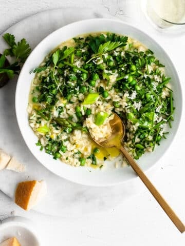 Risotto Primavera (spring risotto) in a white bowl garnished with peas, asparagus and fresh herbs.