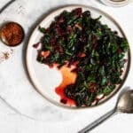 sauteed greens on a white plate garnished with chili flakes