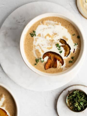 Wild mushroom soup drizzled with cream and sprinkled with fresh thyme in a white bowl